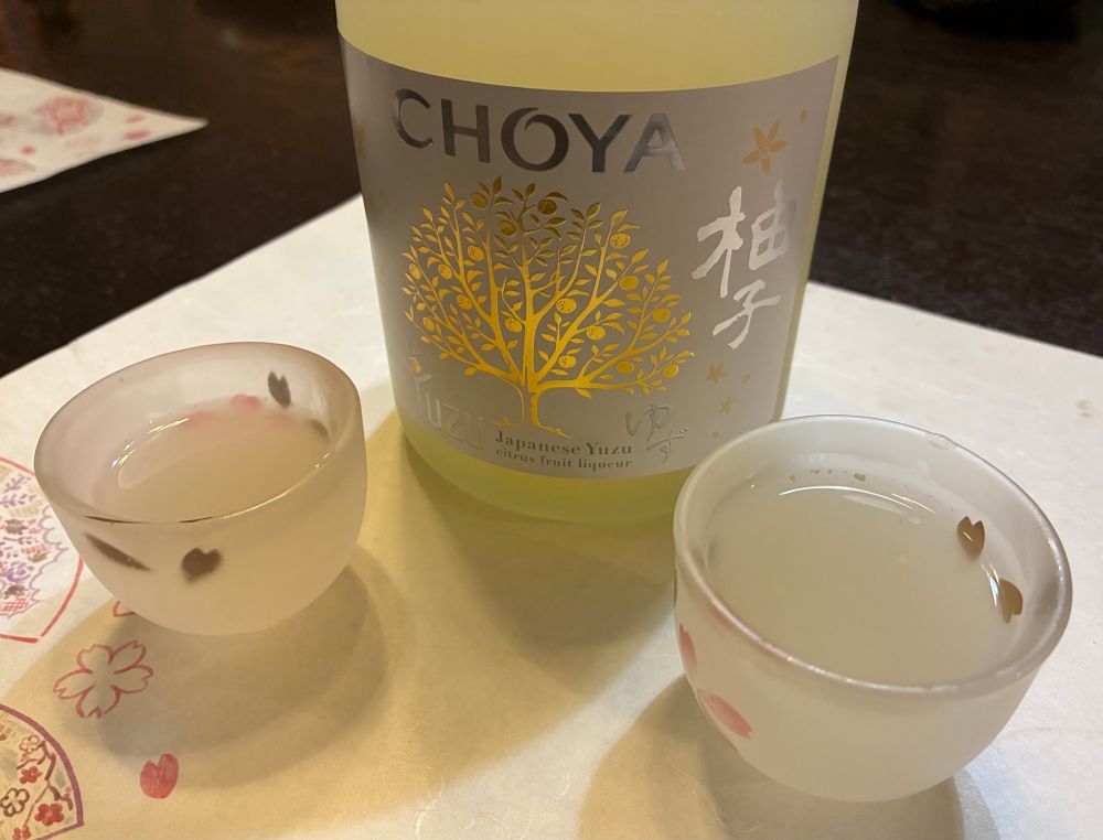 A bottle of Choya yuzu liquor and two filled ochokos sit on the table.