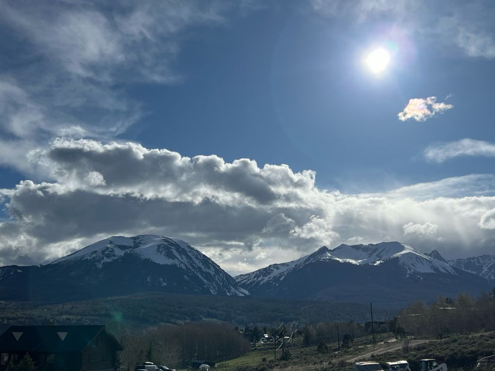 a bright sun against a blue sky and dramatic clouds over snowy mountain peaks