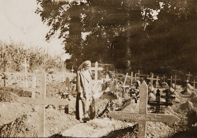 Black and white photo of a graveyard filled with wooden crosses. A nurse stands besides one of the graves