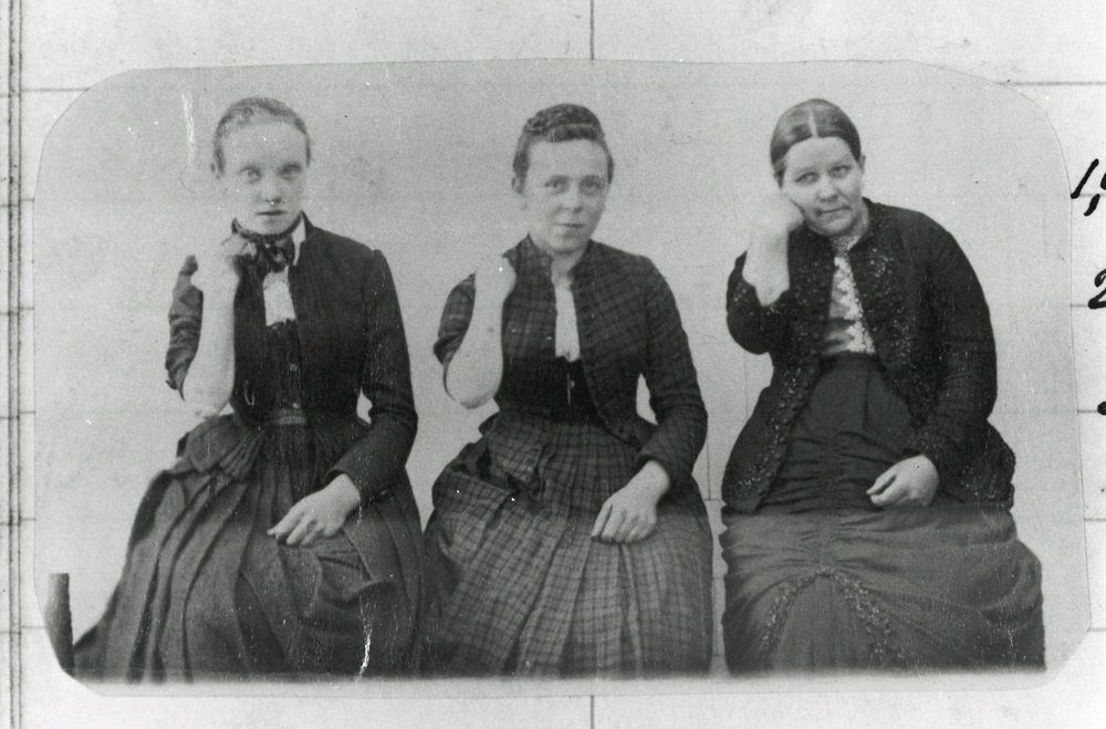 Black and white photo of three women their arms bent towards their face