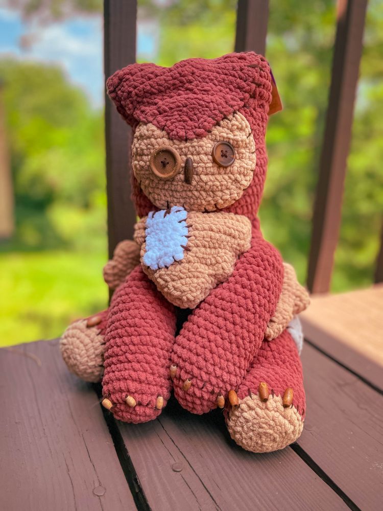 a crocheted owlbear with button eyes sitting upright on a balcony
