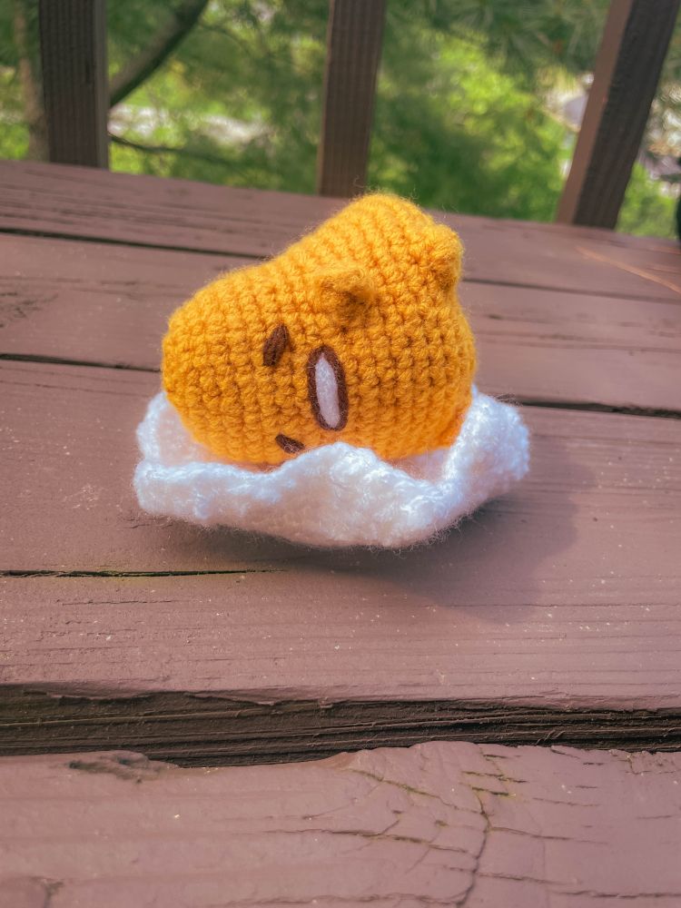 A crocheted gutetama laying on their side

