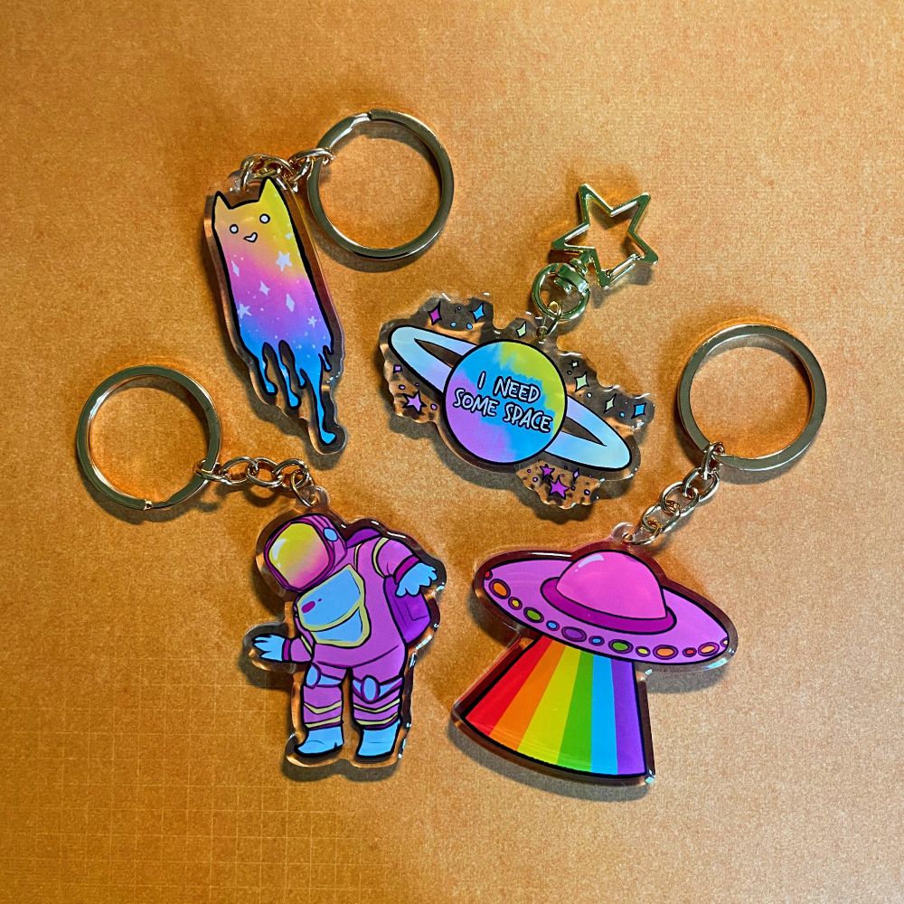 keychains of a drippy space cat, a planet that says "I need some space", an astronaut, and a rainbow ufo