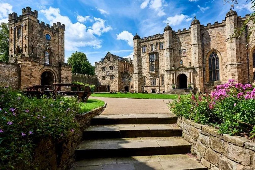 Durham Castle courtyard on a sunny day - a patch of green grass surrounded by historic buildings.