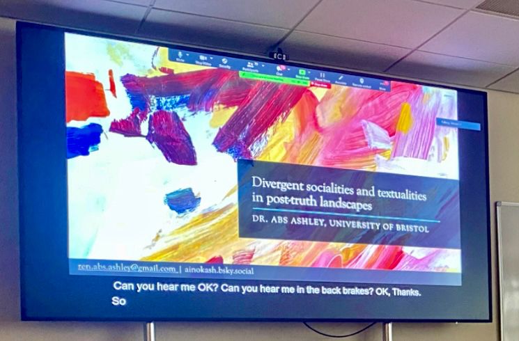 A PowerPoint slide showing a brightly coloured abstract painting with text that reads 'Divergent socialites and Textualities in post-truth landscapes, Dr Abs Ashley, University of Bristol'. 