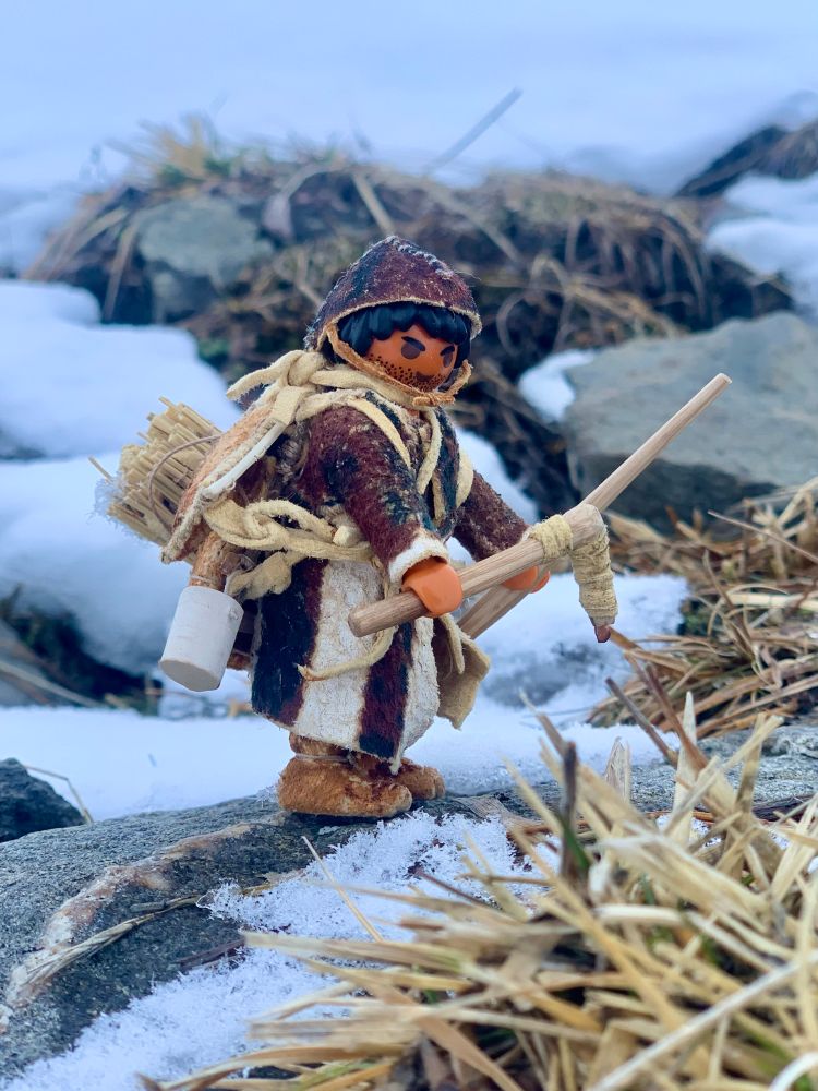 Playmobil figure kitted out as Ötzi the iceman on a rock surrounded by snow.