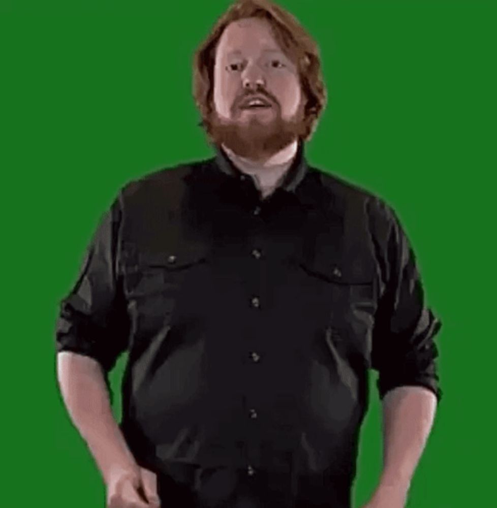 a man with a beard is standing in front of a green screen holding a large letter b .