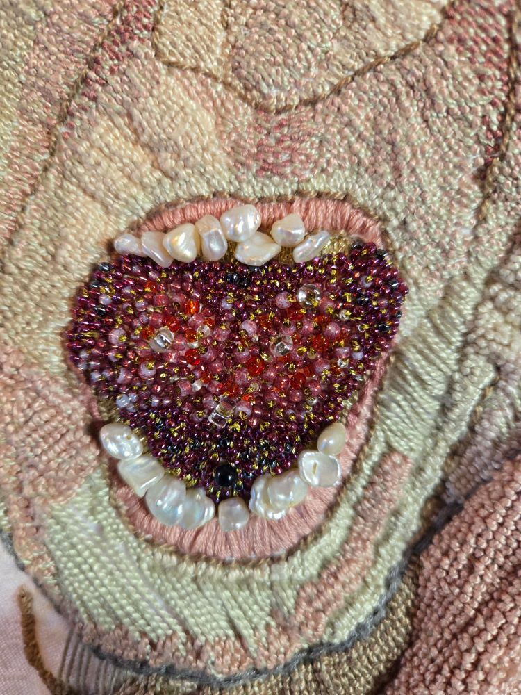 a close up of an embroidered open mouth, pearls as teeth, red beads inside