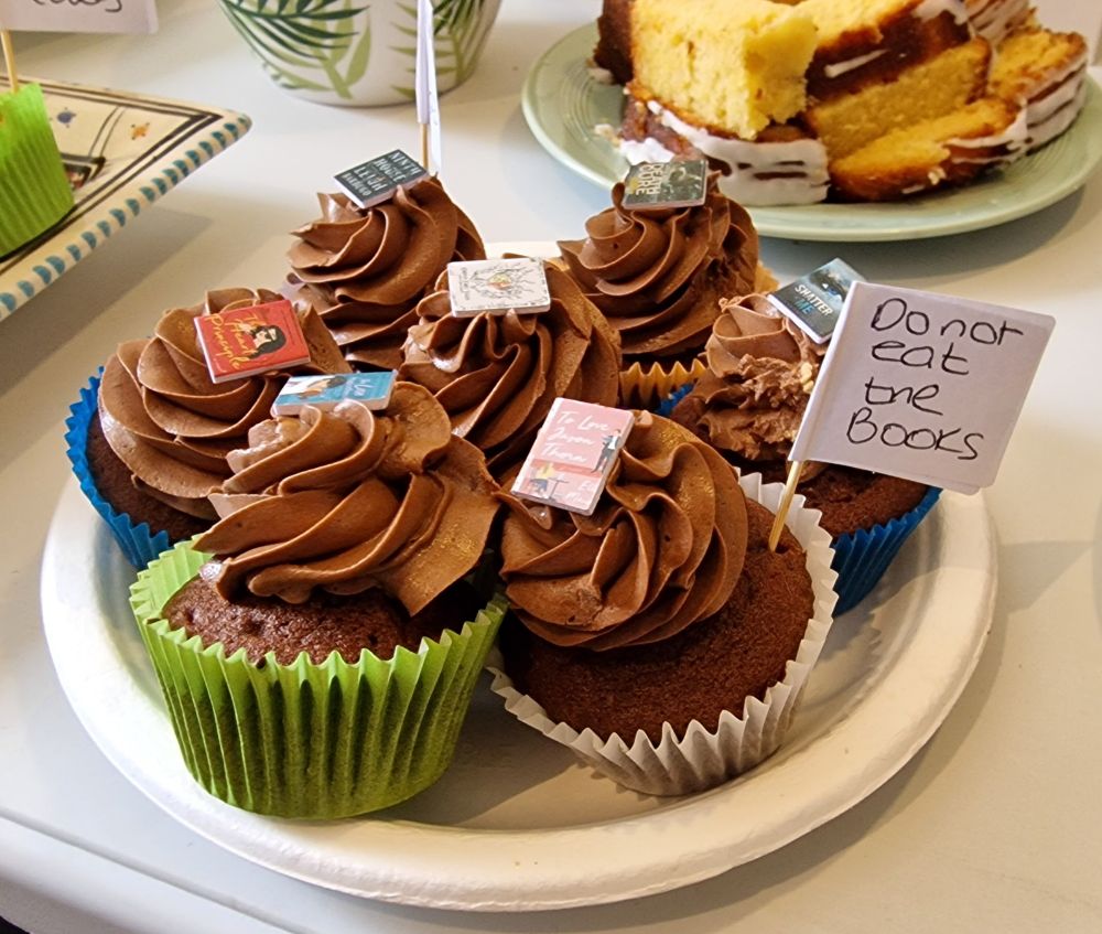 A plate of cupcakes with miniature book covers embedded in the icing. A small sign attached to a cocktail stick says "do not eat the books"