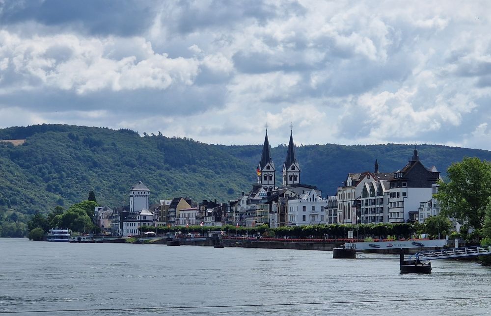A view across the water to a small town dominated by two pointed church spires, with wooded hills in the background 