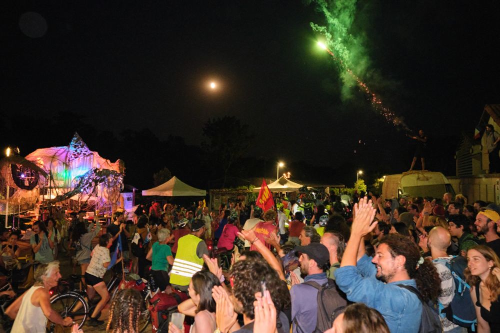 A convoy of activists from Brittany on their bikes is greeted with cheers and applause, a man shot a firework in Melle, France on July 18, 2024. The water village, organized by Bassines Non Merci and the Soulevements de la Terre collective. Adrien Auzanneau / Hans Lucas #hanslucas