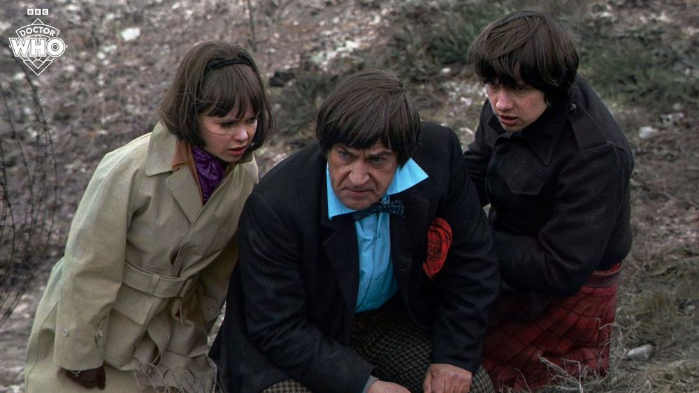 The Second Doctor, Jamie and Zoe all huddled on the rocky ground. This is a colour image from THE WAR GAMES
