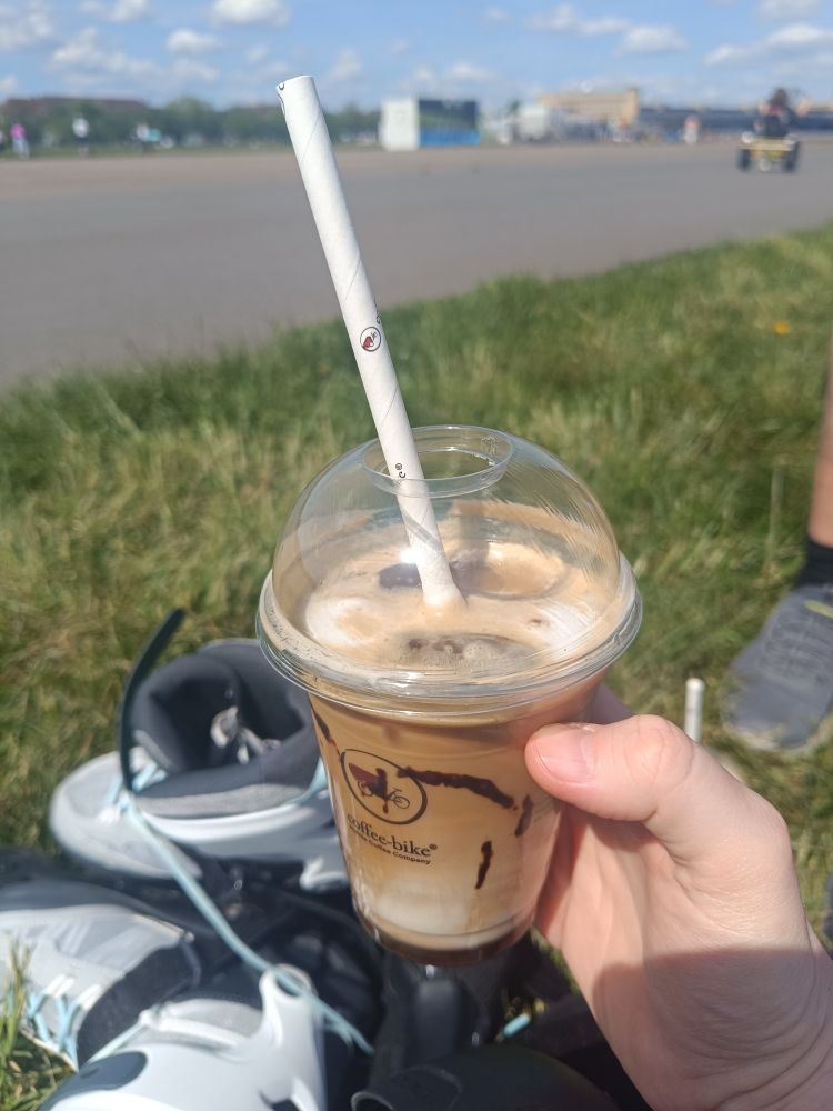 Ein Eiskaffee im Becher, im Hintergrund die Inline Skates auf der wieder bei strahlend blauem Himmel