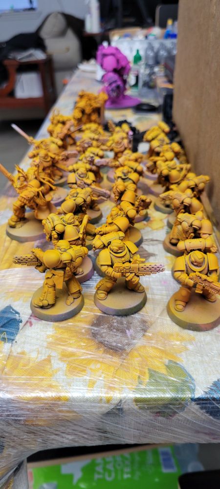 25 space marine minis from Warhammer 40,000 painted fully yellow with a pink dreadnought in the background awaiting highlighting and base coating.