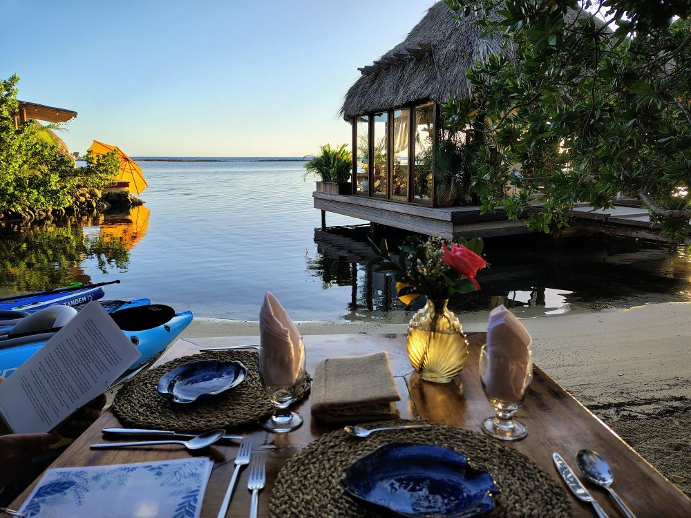 Table setting looking out across the ocean next to a cute bungalow sticking out in the water at sunset 