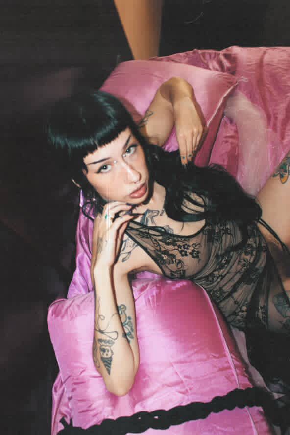 Pony lays back, dress exposing her bush, ponytail cascading down her side and hands by her face