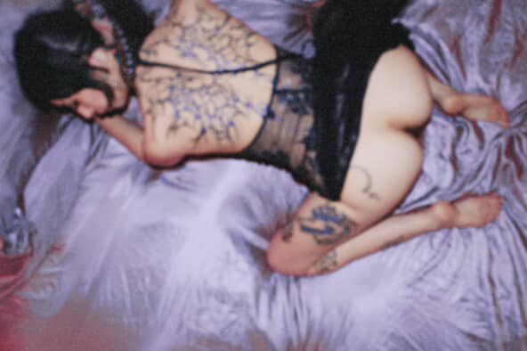 Pony in purple silk sheets wearing a black lace dress with low back, on her knees with her dress tossed to the side showing her soft supple ass