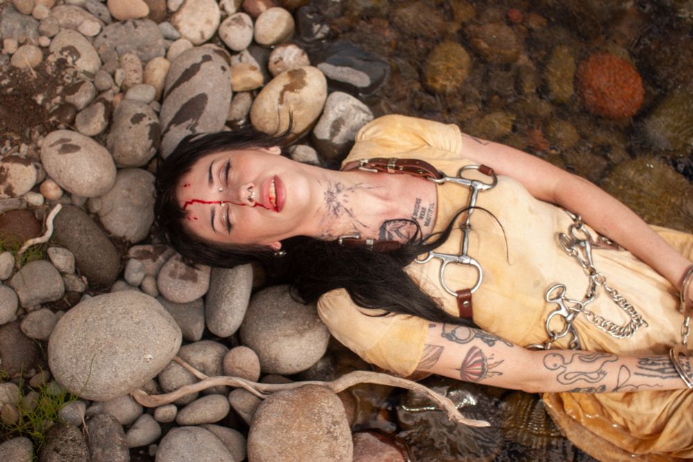 Pony lays back on the shore of the rocky river, blood streaming down her nose into her mouth