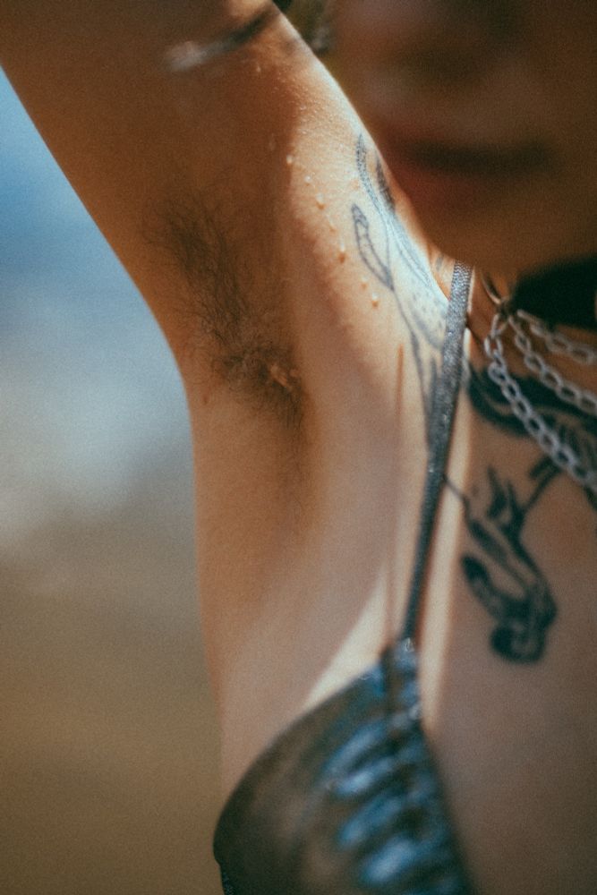 Pony raises their arm to show their hairy pit, water dripping down the side, get out of focus bikini and darling face in the foreground