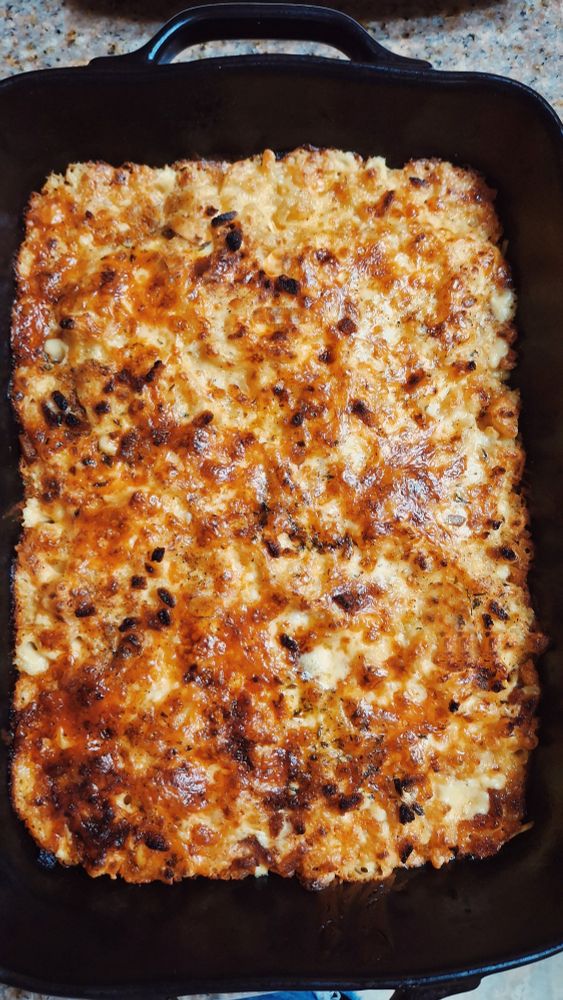 A black casserole dish holds baked three cheese macaroni with a crispy layer of cheese and bread crumbs 