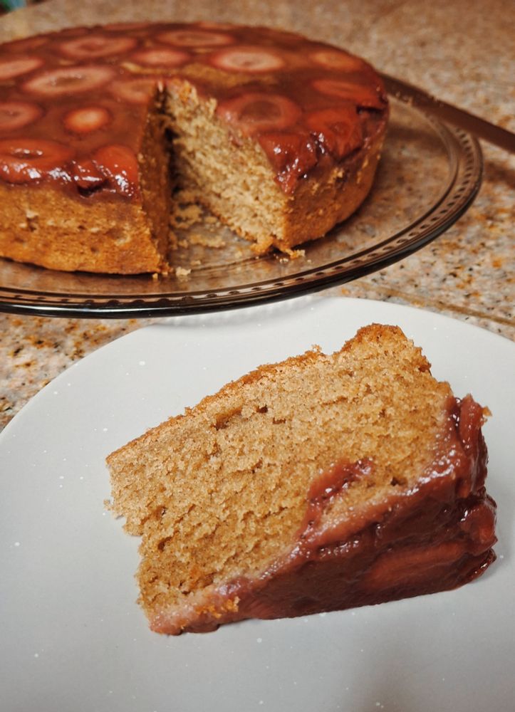 A slice of cake on a small plate sits next to a 9 inch strawberry upside down cake 