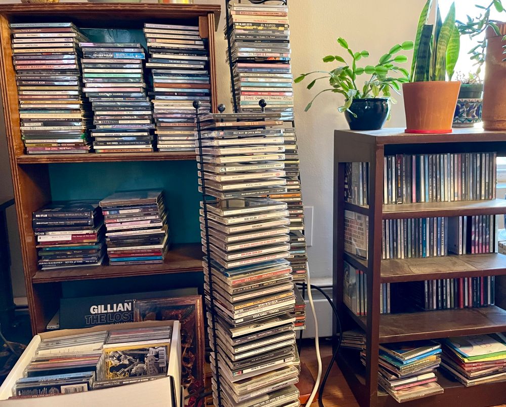 Two small bookcases and two wire racks full of CDs, with a couple of cardboard boxes packed with more
