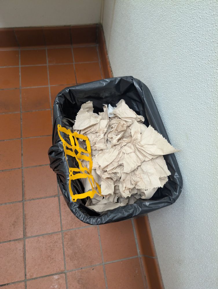 A trash can overflowing with paper towels and a plastic six pack ring