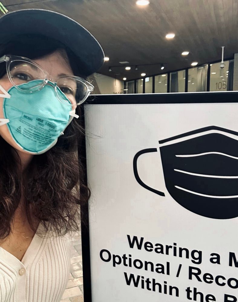 Selfie in 3M 1860 green mask with skin that says "wearing a mask is optional within the building"