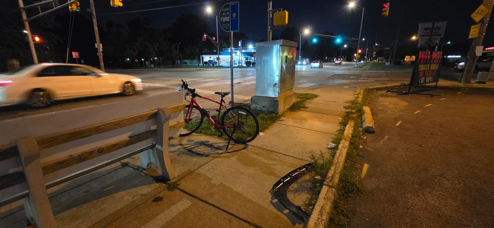 A plastic piece of car trim sitting five feet from a bench at a bus stop.