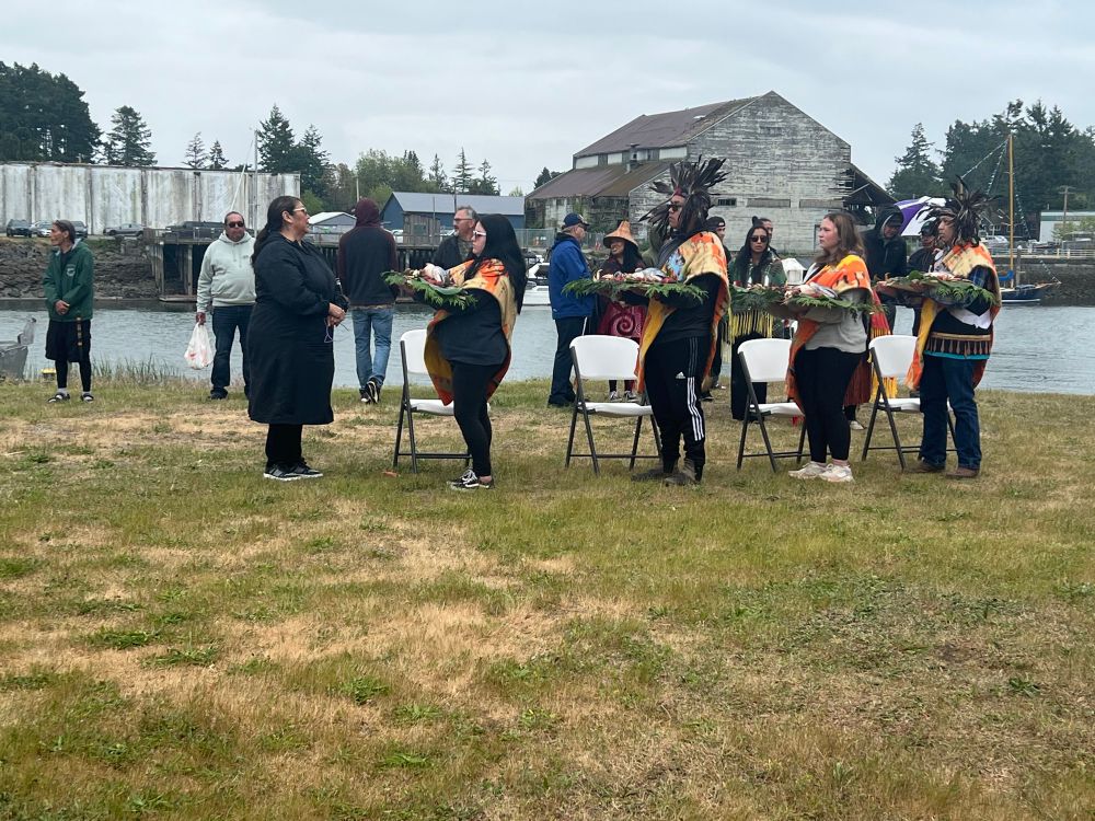 four Tribal youth standing and holding salmon and berries offerings near Swinomish Channel. they are preparing to go the four compass directions to return the offering to water bodies in each of the directions.