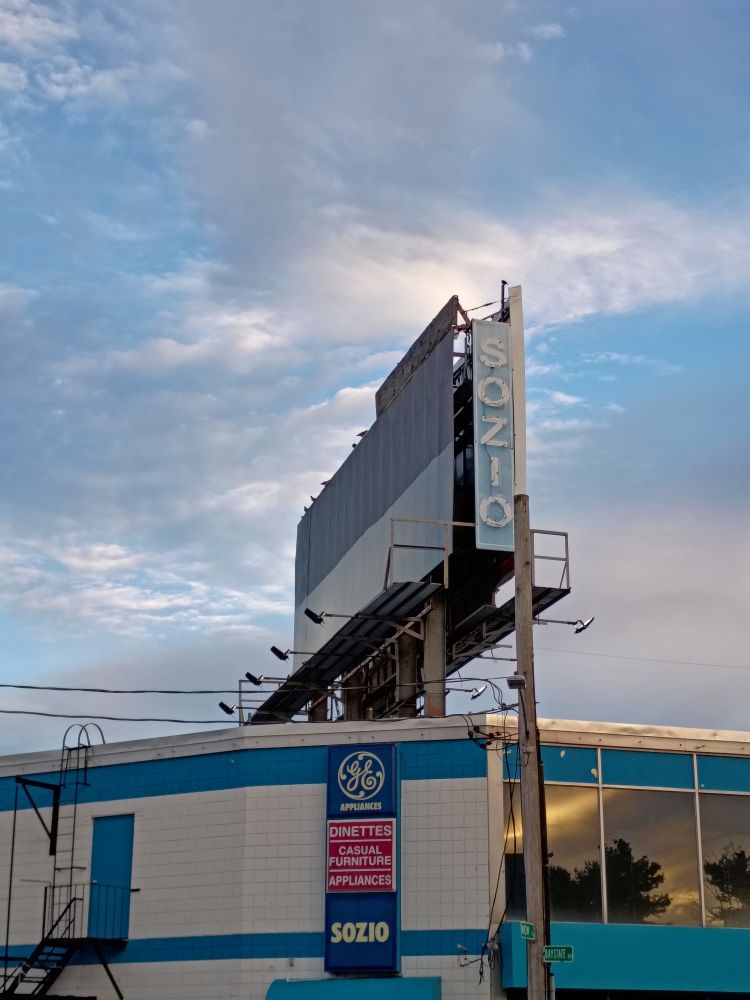 Cool blue sign/billboard that says SONZIO. It definitely used to be lit with neon lights. It matches the golden hour sky behind it