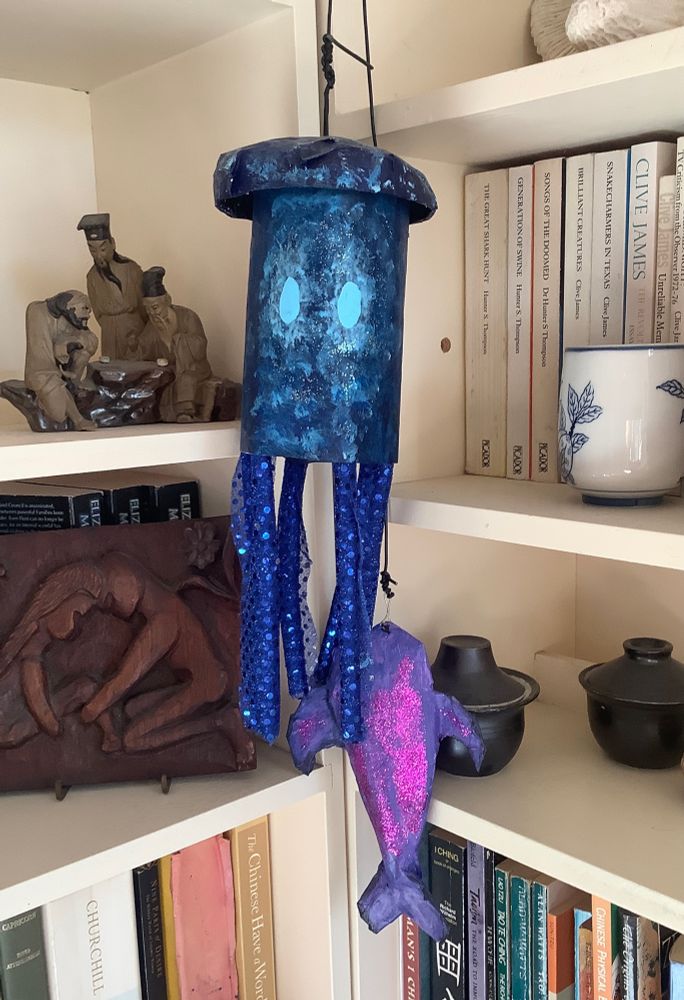 paper mache cosplay items hanging near a bookshelf :Stardew Valley midnight squid and midnight carp