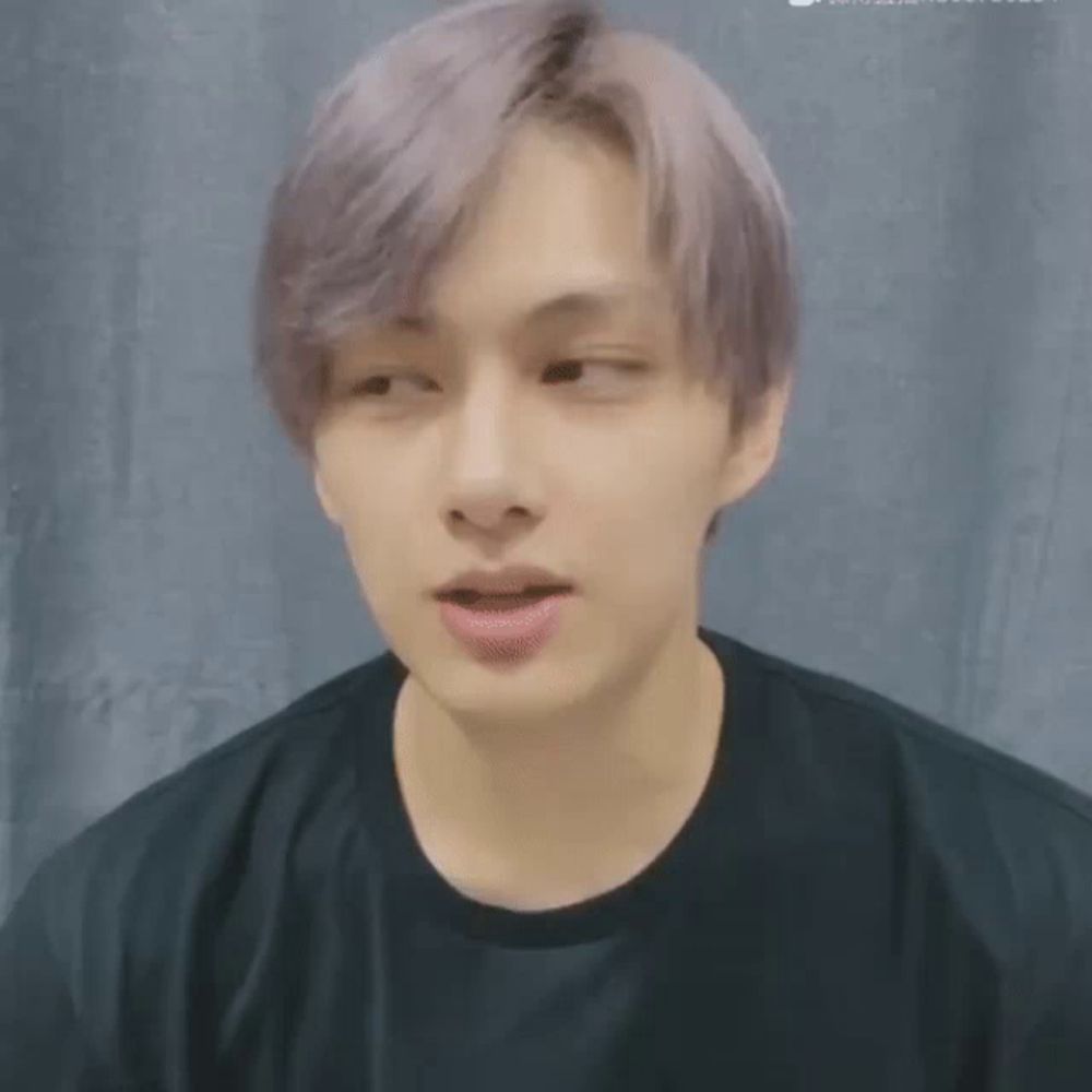 a young man with purple hair and a black shirt is making a funny face .