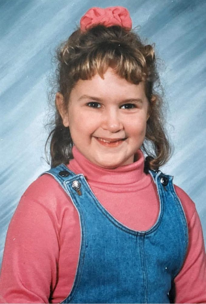 A photo of me Sara when I was about 6 or 7 years old. I'm in a blue jumper, pink shirt ,my hair is up and there's a blue background.