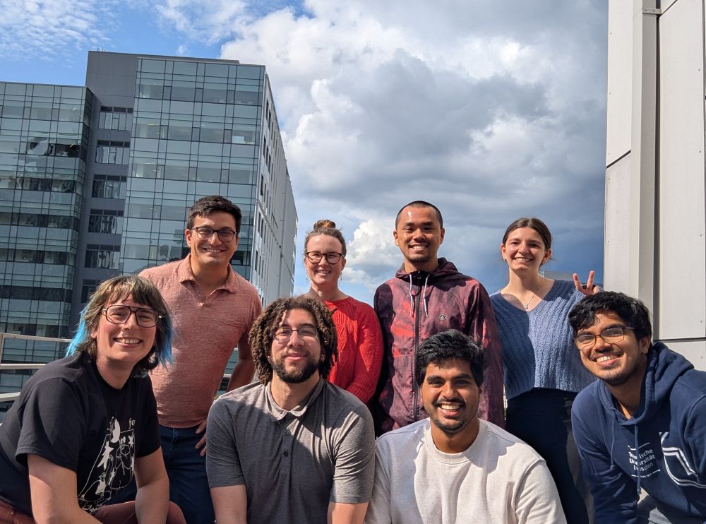 The Matsulab smiles in front of the Seattle skyline. Tall people are squatting in the front, and shorter folks are in the back row.