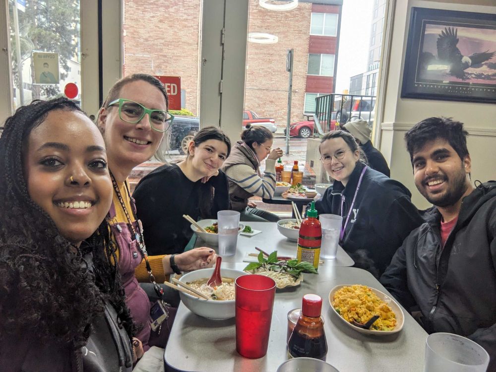 Lab members Hanna, Valerie, Emma, Maggie, and Abhi sit around a table with Vietnamese food.