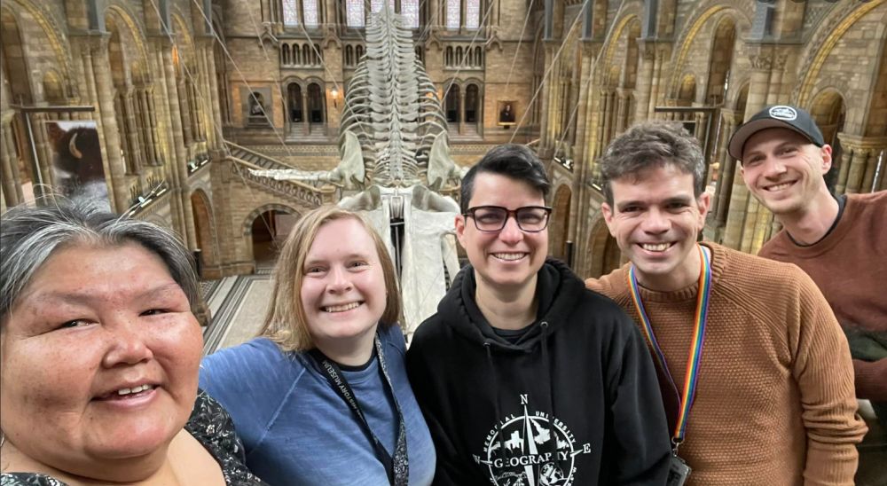A group of five people in a museum with a whale skeleton behind. 