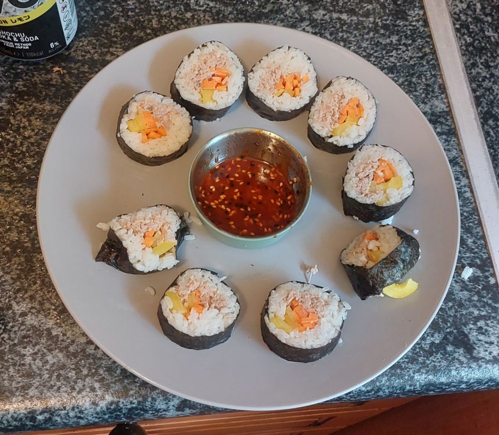 Moderately well made kimbap arranged in a circle on a plate with bibimbap sauce in a dish in the middle