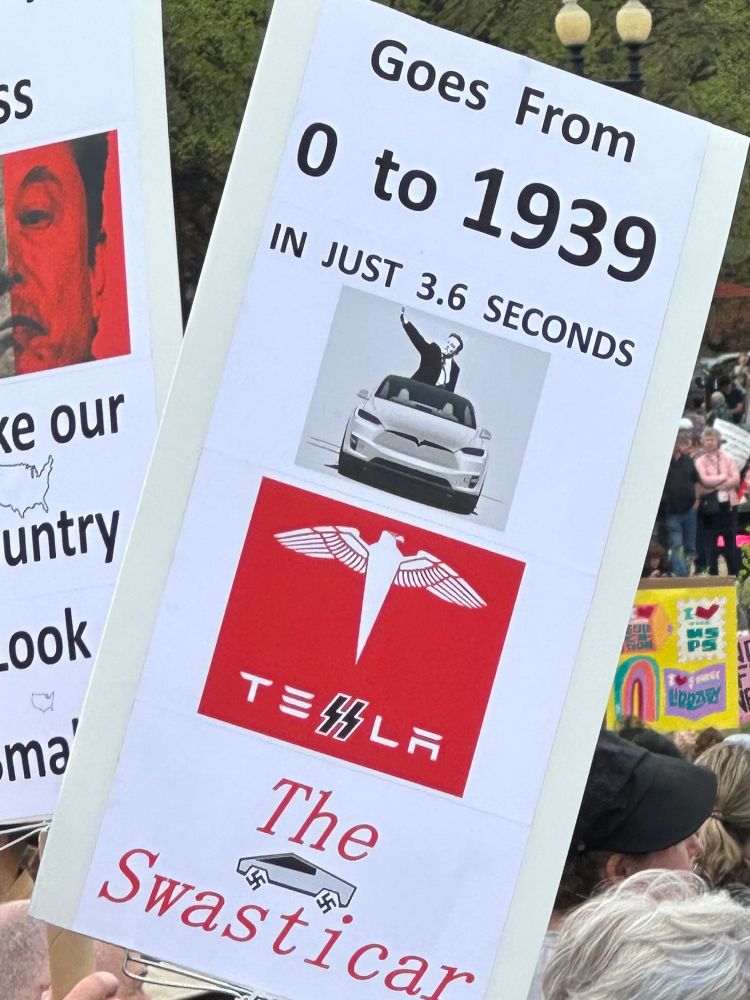 A protester’s sign “0 to 1939 in just 3.6 seconds the Tesla swasticar.” 