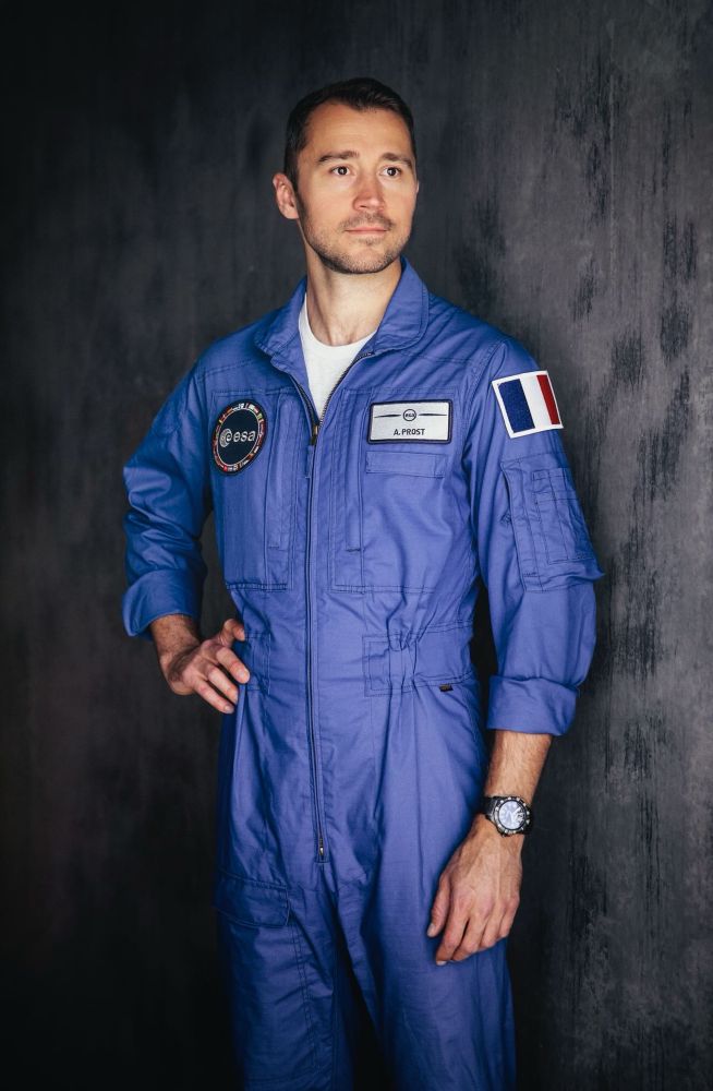 Photo d’Arnaud Prost, astronaute de réserve de l’ESA en combinaison d’astronaute. Il tient une main sur sa hanche et regarde au loin.