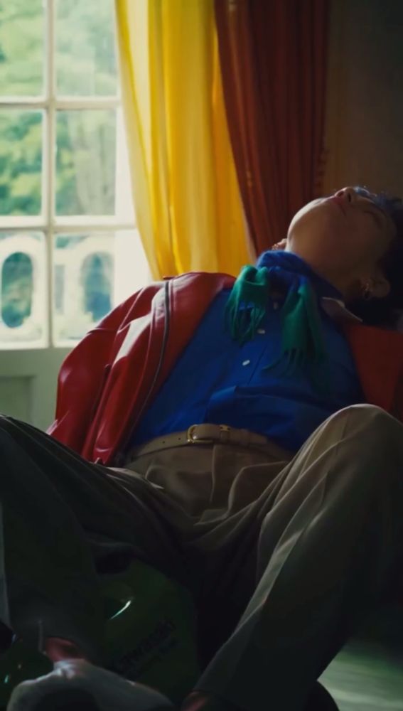 taehyung sitting leaning back during his wkorea shoot wearing red blue and khaki 