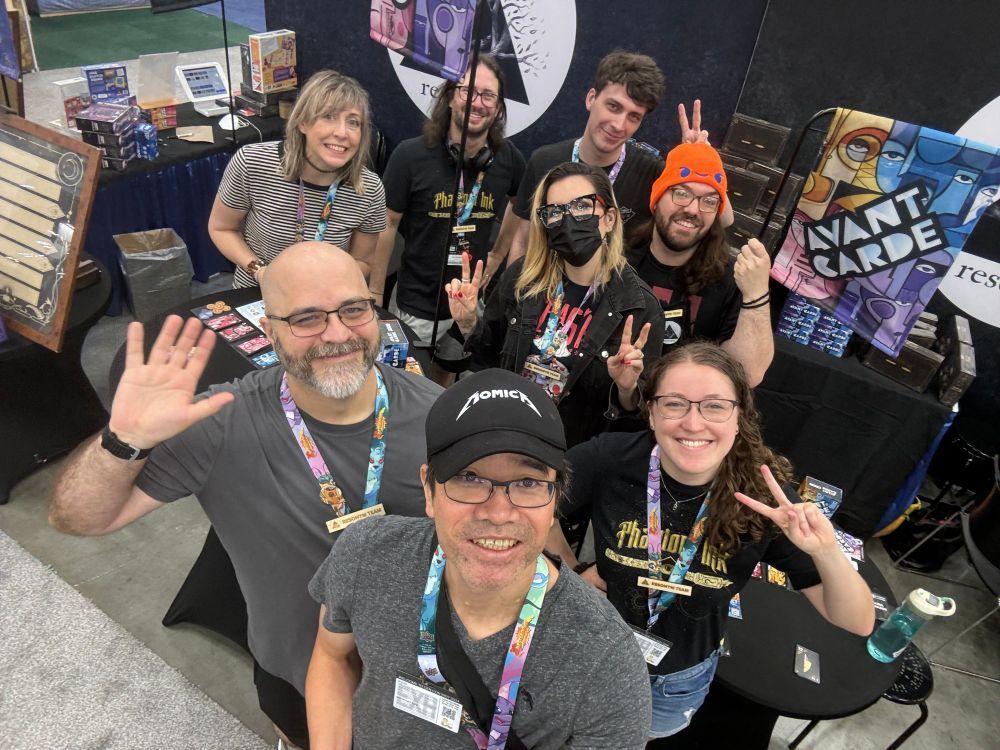 Resonym booth team from Gen Con 2024 posing for the camera with the booth in the background. Max has a pole in front of his face