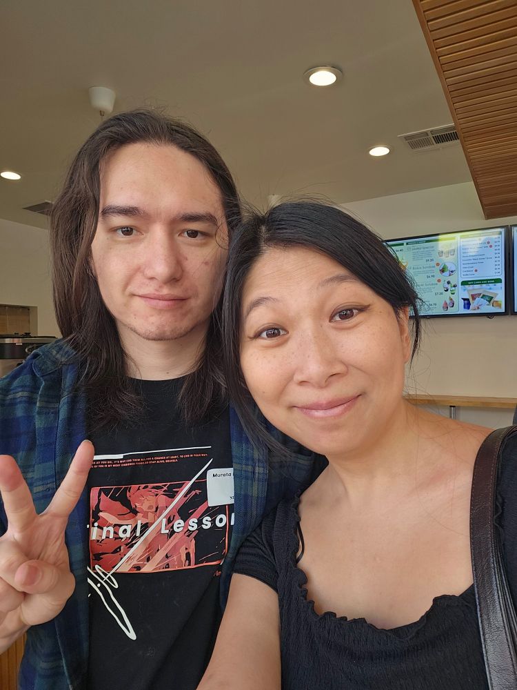 A couple smiling at the camera. The person on the left is holding a hand in a peace sign.