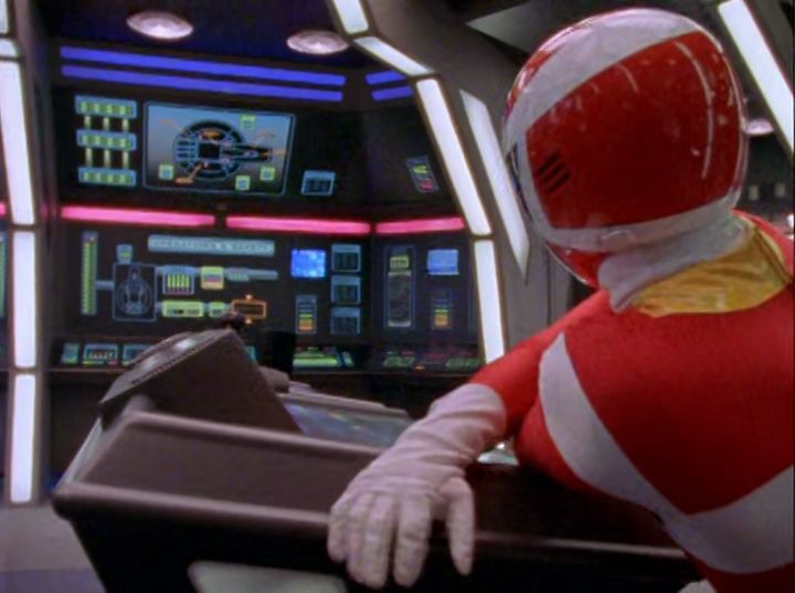 the red ranger leaning on the cockpit console with several screens in the background showing ship status