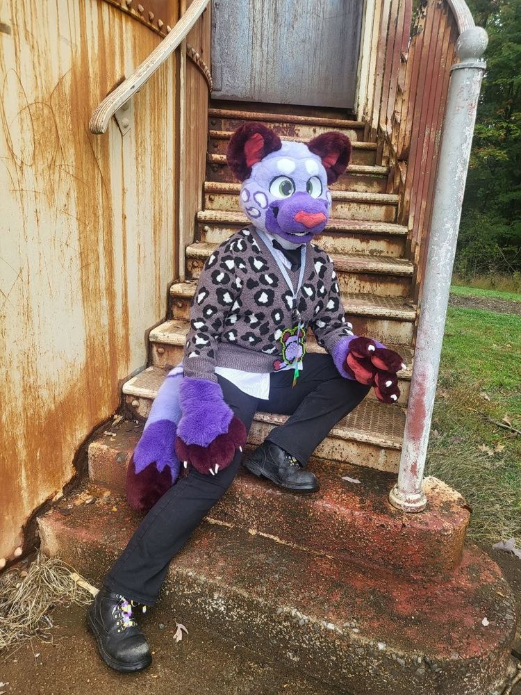 A person in a purple snow leopard fursuit posing on some rusty stairs
