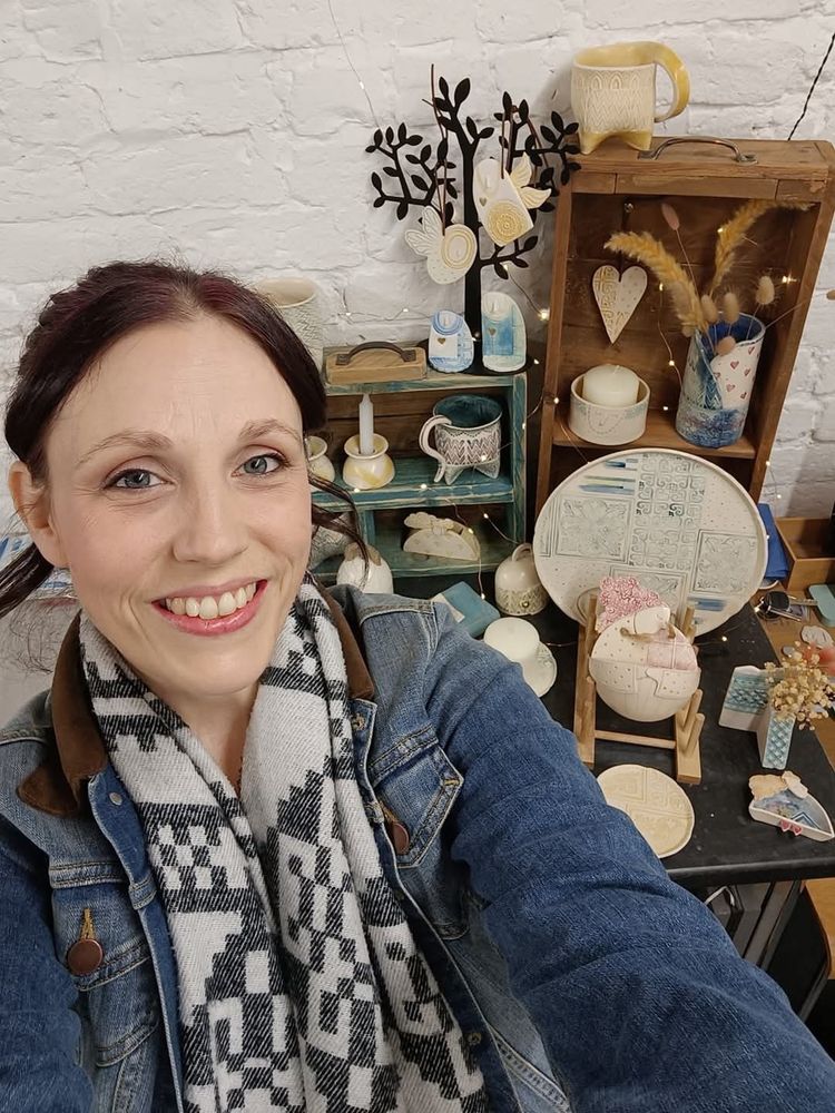 Image of me (Laura Jane) in front of a selection of my handmade ceramics in my pottery studio.
