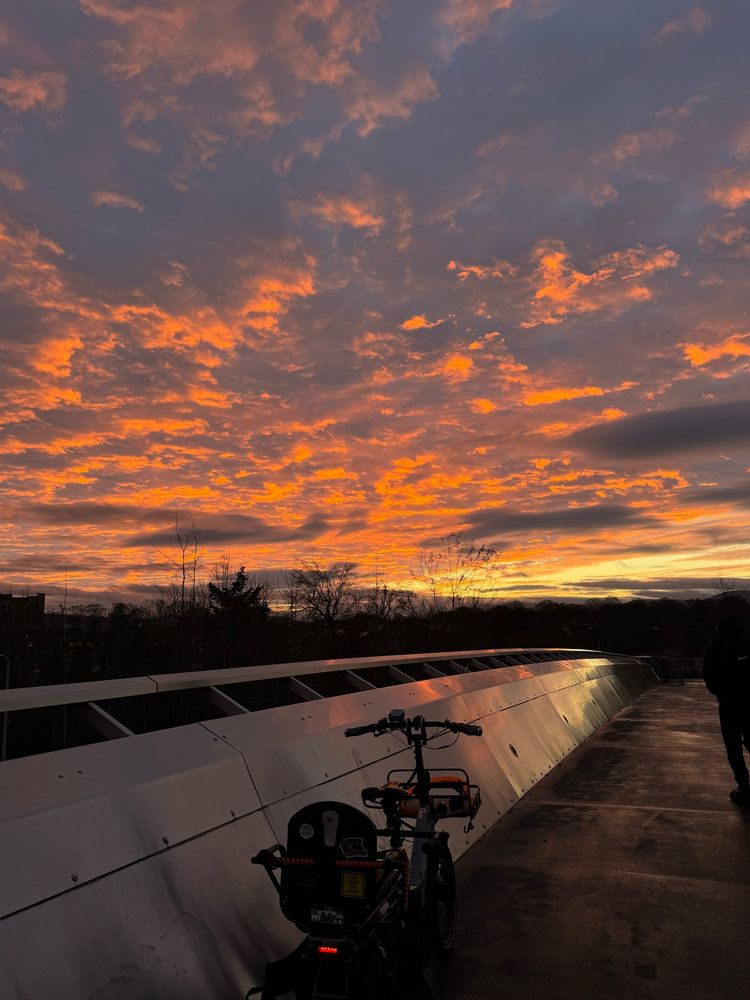 Picture of orange glowing clouds at sunset, with a bridge and tern cargo bike in the foreground