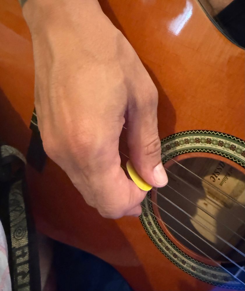 Männerhand mit gelbem Plektrum beim Gitarre zupfen