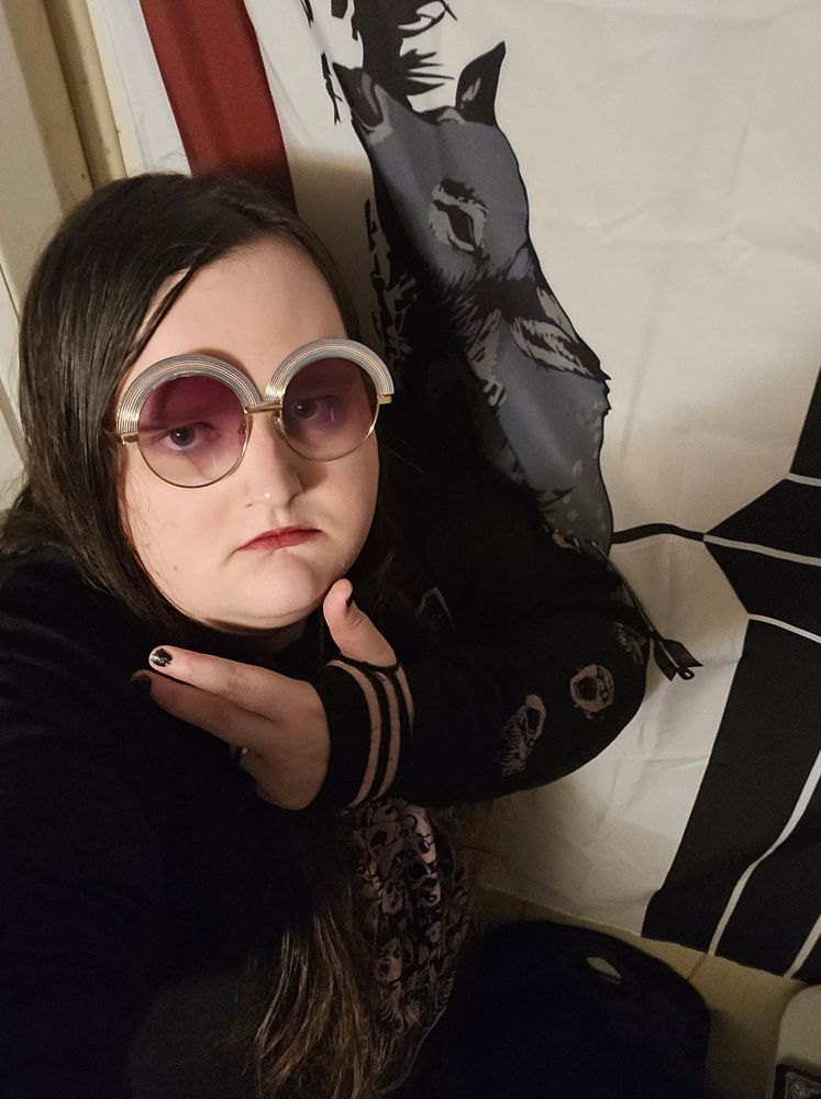 Me wearing pink glasses and pink and black sleeves with a pink black and blue junji ito shirt 