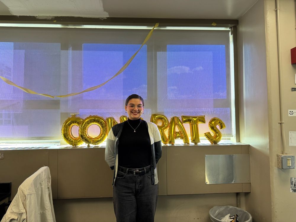 Amelia Ryan, a 4th year PhD student, stands in front of a “Congrats” balloon arrangement to celebrate her passing her candidacy exam.